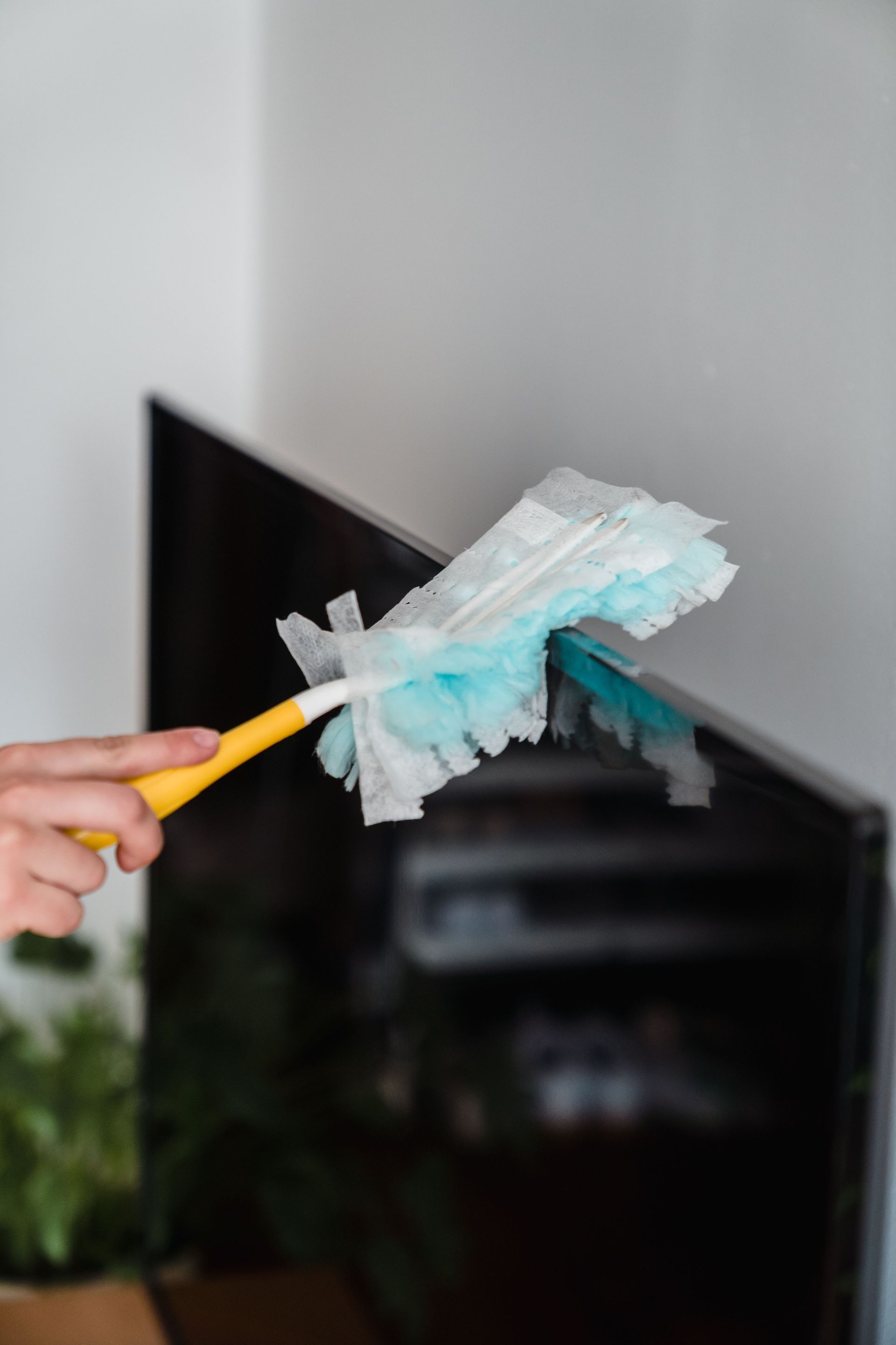 Close-up of a hand dusting a TV screen with a blue feather duster indoors.