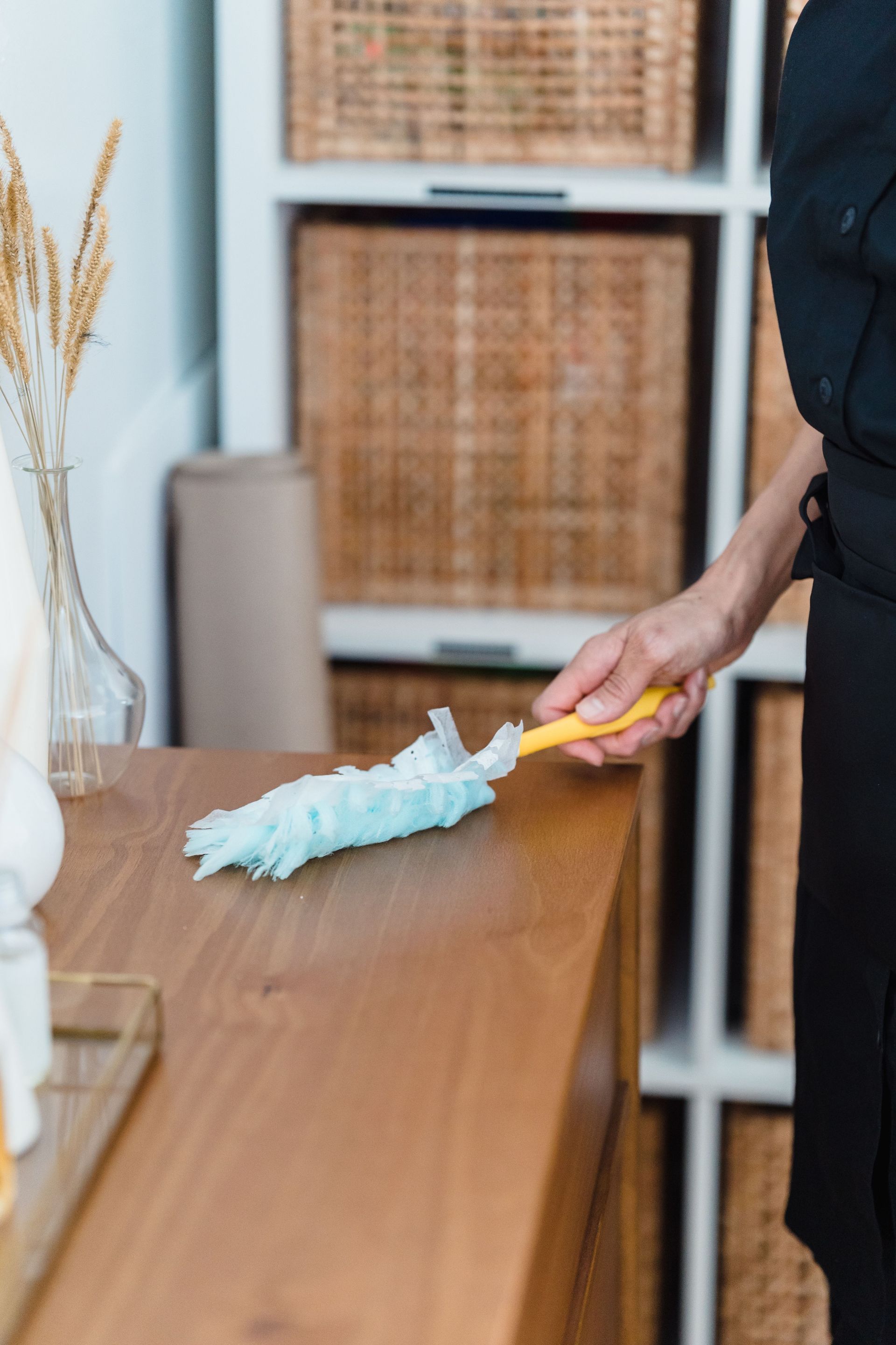 A woman in a black apron dusts a wooden dresser, highlighting household chores and cleanliness.