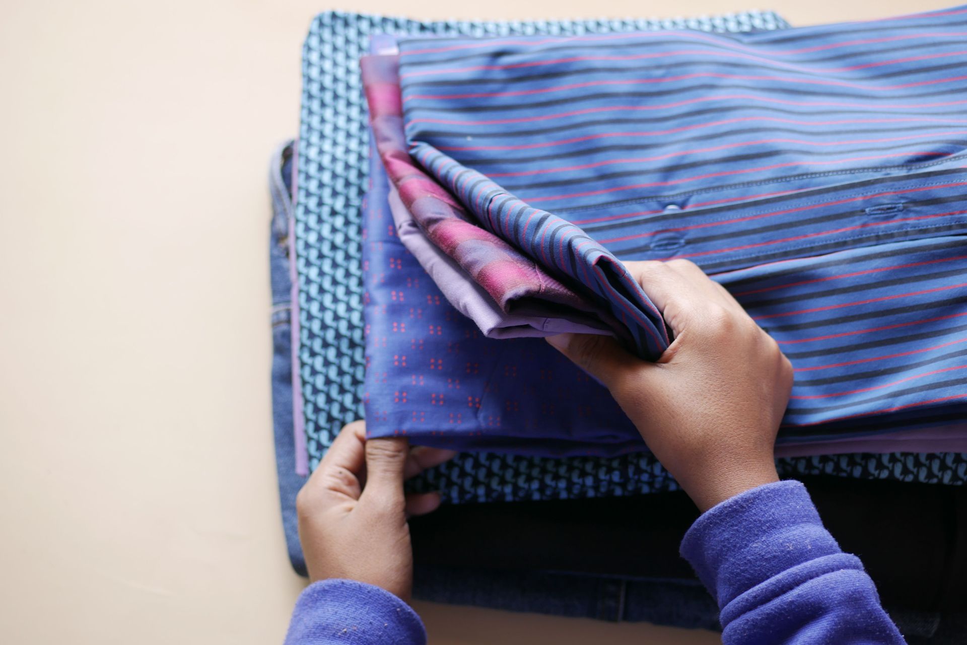 Hands folding a pile of colorful patterned shirts arranged neatly in a high-angle view.