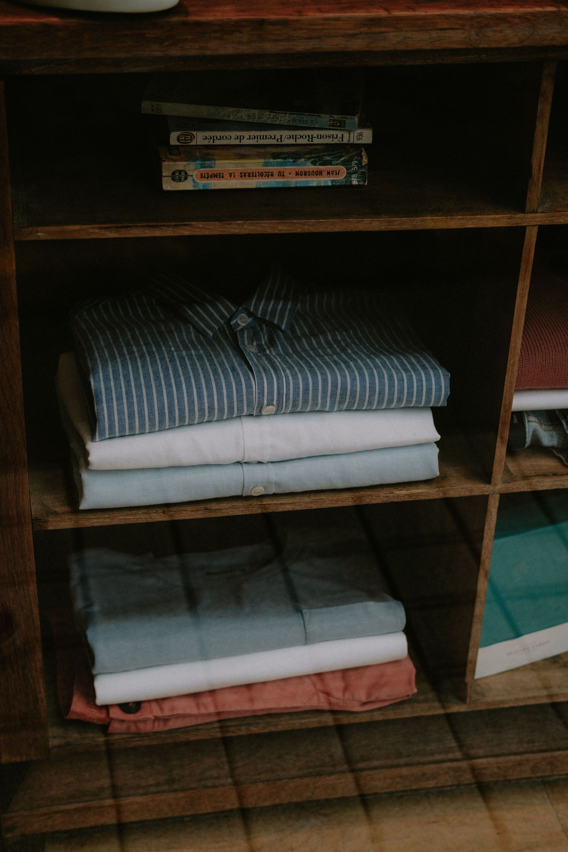A tidy wooden shelf with neatly folded clothes and stacked books.